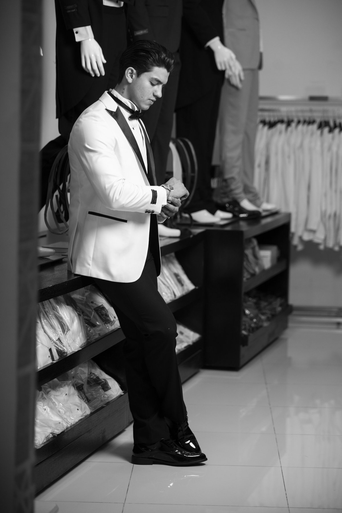 Man in white blazer and black bow tie adjusting his outfit in a clothing boutique dressing room, black and white photography