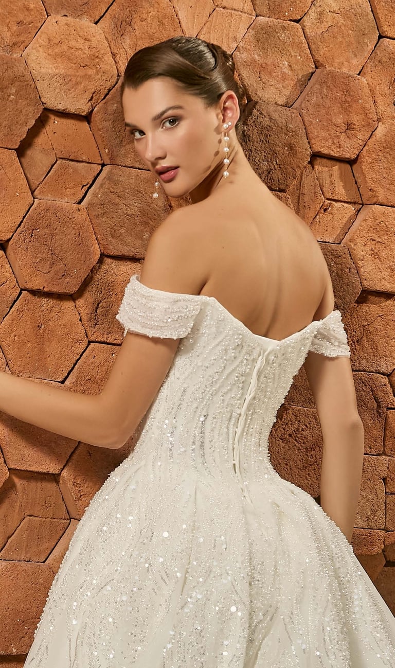 Novia con vestido off-shoulder con beads contra pared de ladrillo
