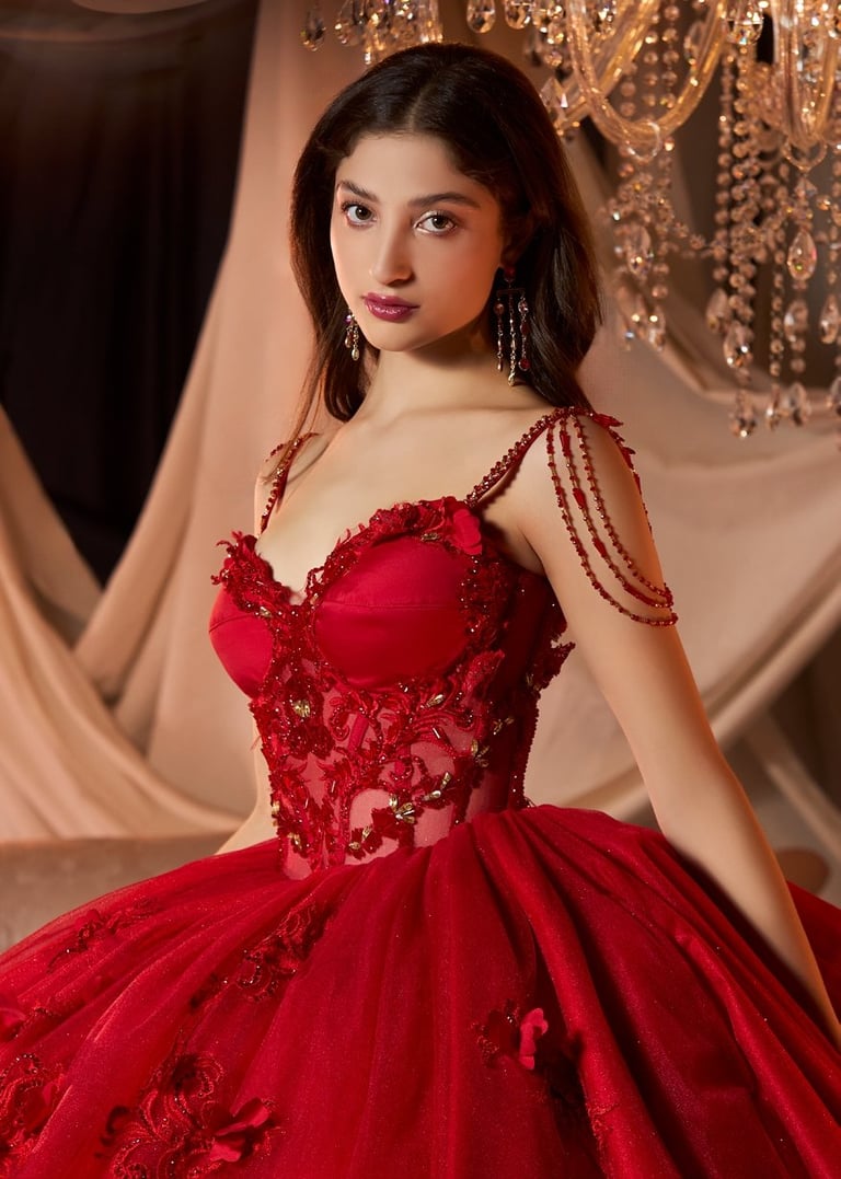 Quinceañera con vestido rojo ball gown con beads y detalles de cadena en hombros contra fondo dorado