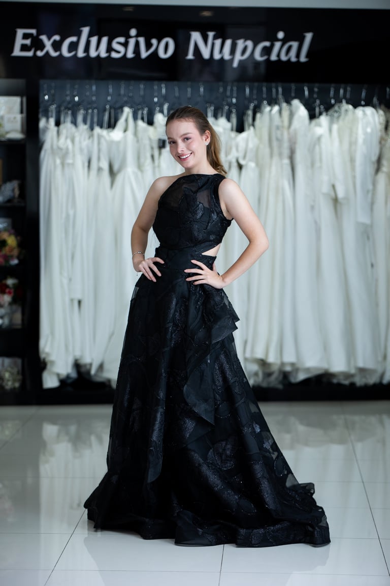 Mujer joven con vestido formal negro en tienda nupcial con vestidos blancos detrás