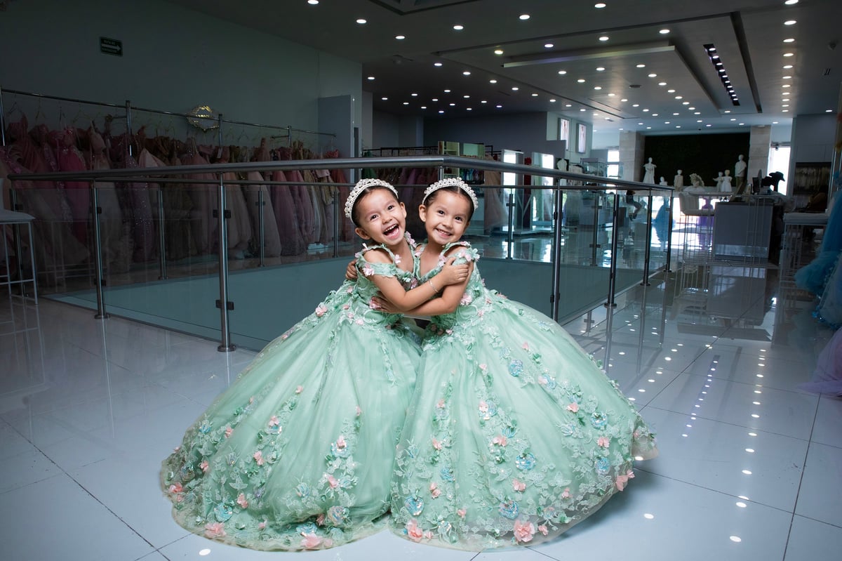 Dos niñas jóvenes en vestidos de bola mint green combinando estrechándose en boutique nupcial