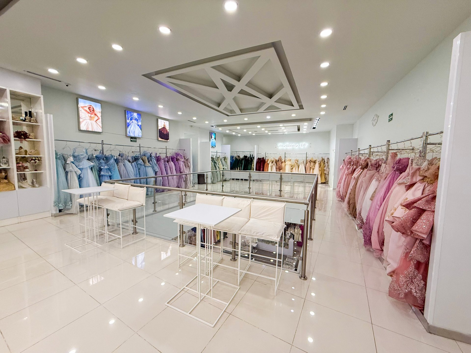 Interior de tienda de moda al por menor con piso de loseta blanca, vestidos colgados en percheros, mesas de exhibición y estantes