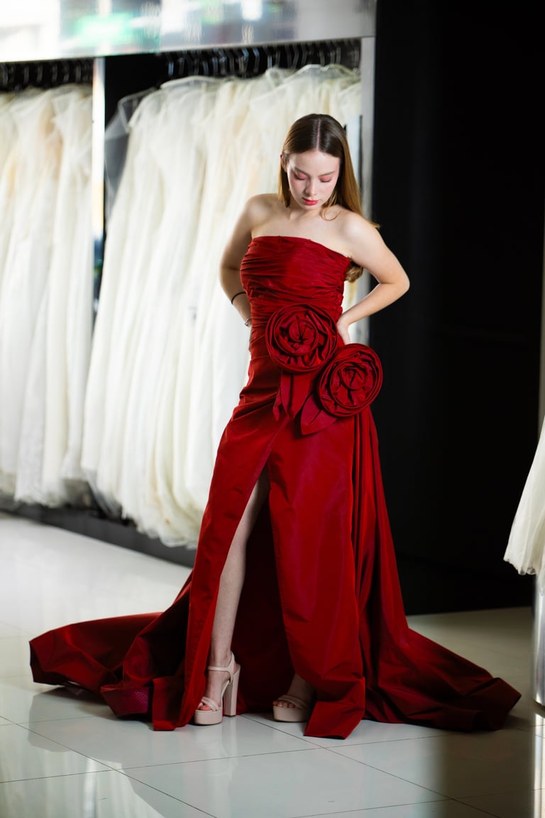 Mujer con vestido rojo strapless con detalles florales y.slits alto en tienda nupcial con vestidos blancos