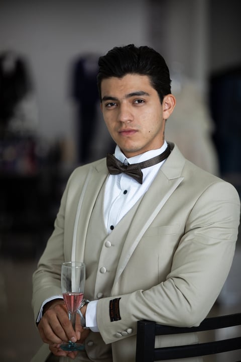 Young man in formal beige suit and bowtie holding champagne glass at an elegant event