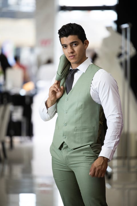 Man in green vest suit with white dress shirt and black tie, holding jacket over shoulder in modern indoor setting
