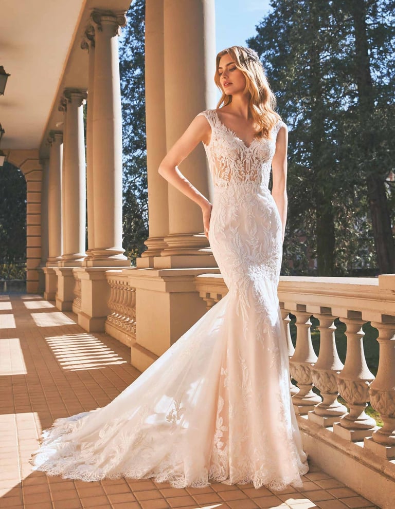 Woman in white lace mermaid wedding dress standing on a classical columned terrace with trees in background
